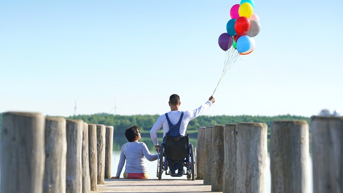 Ein Mann hält bunte Luftballons und die Hand seiner Freundin, die mit ihm auf einer Brücke ist. Quelle:  © Jenny Sturm/stock.adobe.com
